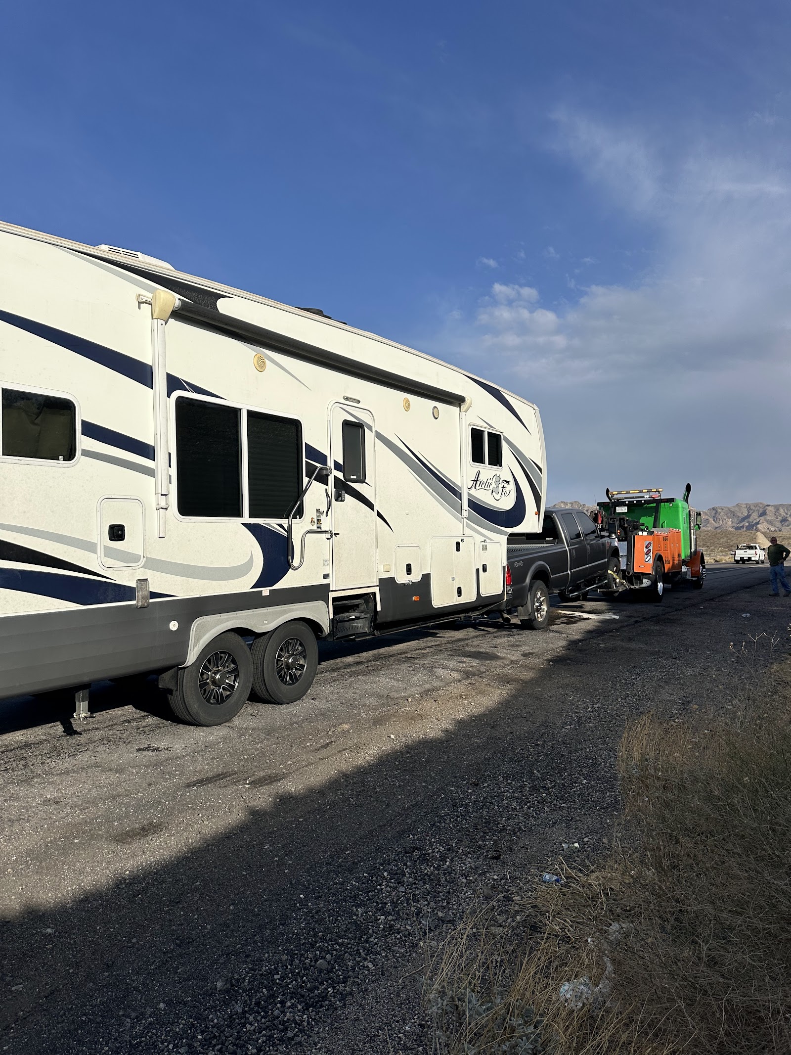 Fifth-wheel Arctic Fox RV and pickup being serviced by a tow truck on a desert roadside