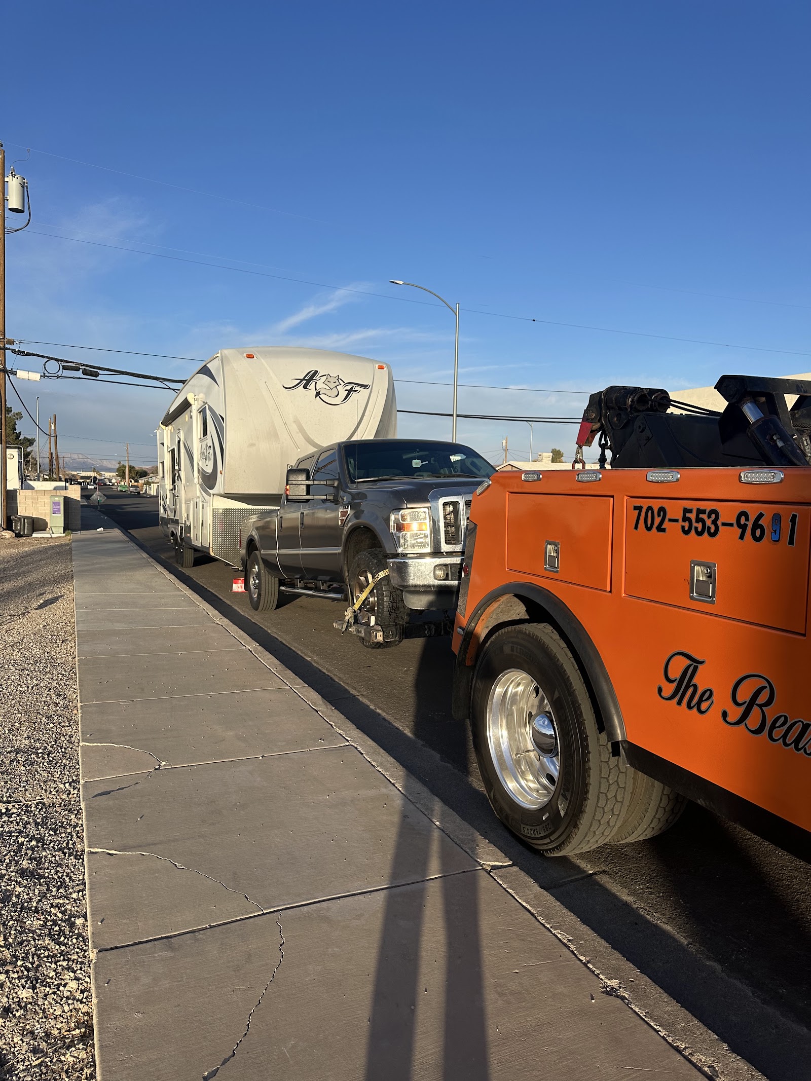 Orange wrecker towing a pickup that is pulling a fifth-wheel RV