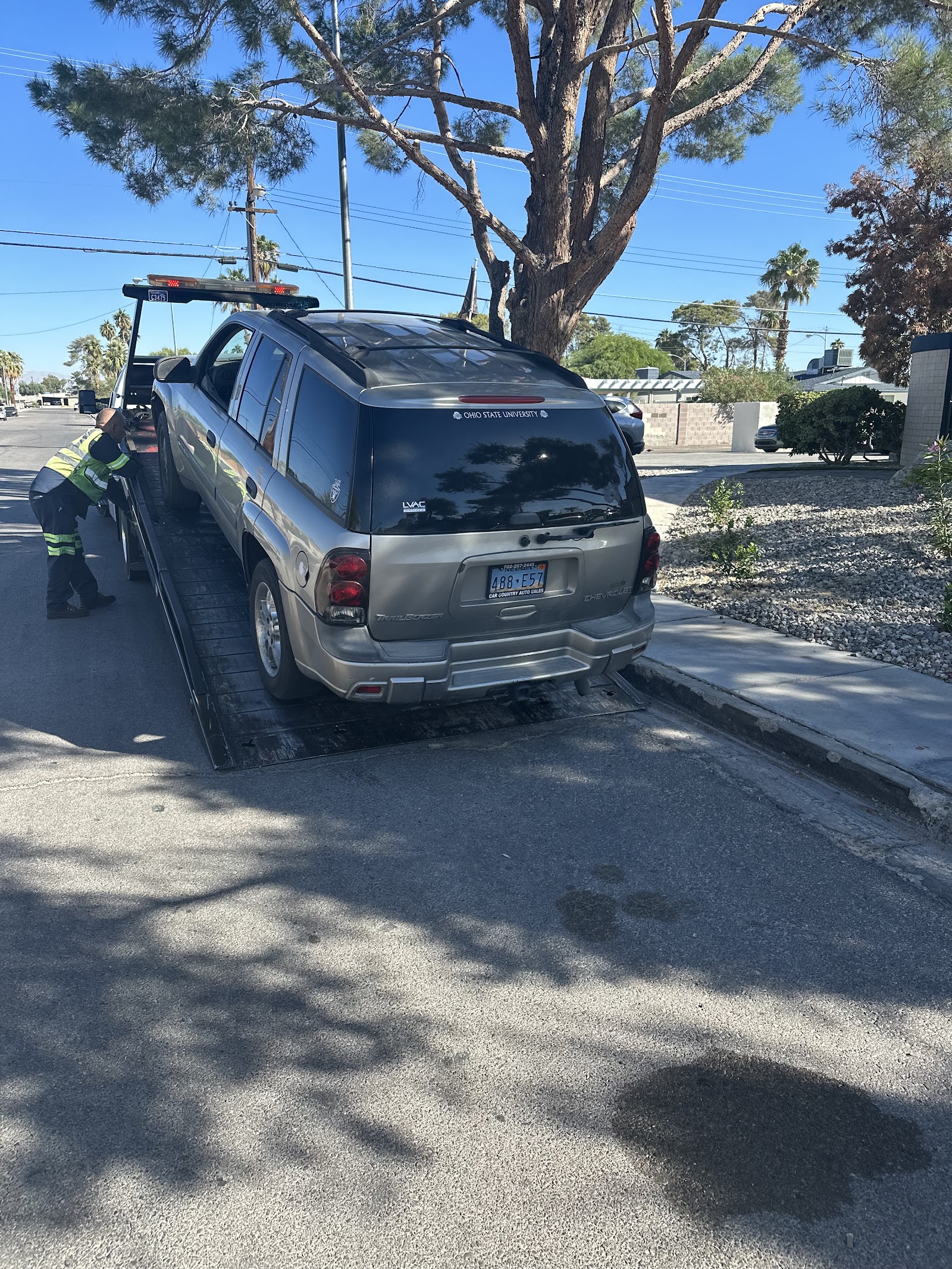 Worker in high-vis vest loading a Chevrolet TrailBlazer SUV onto a flatbed tow truck