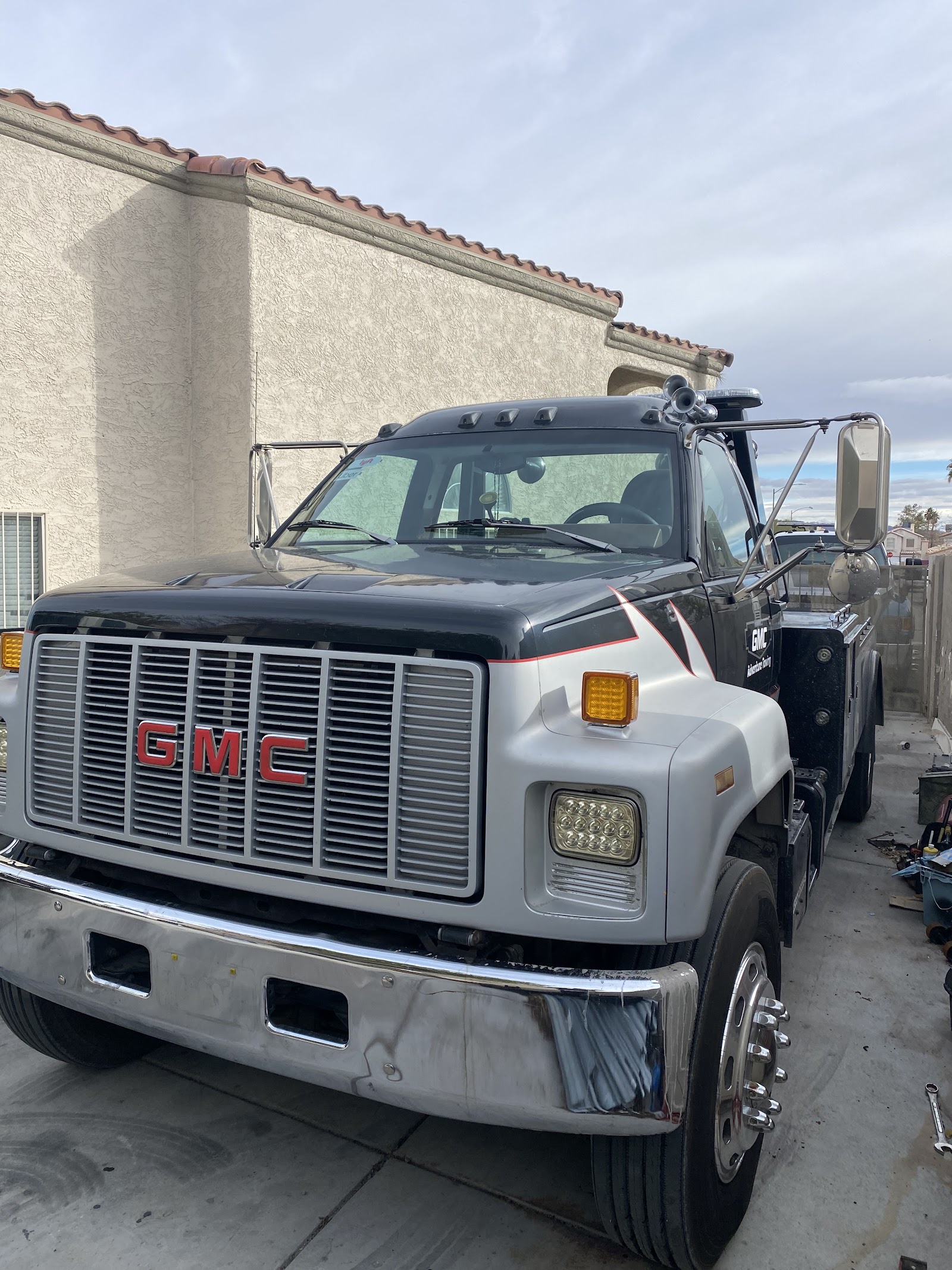 Black and silver GMC medium-duty tow truck parked beside a building