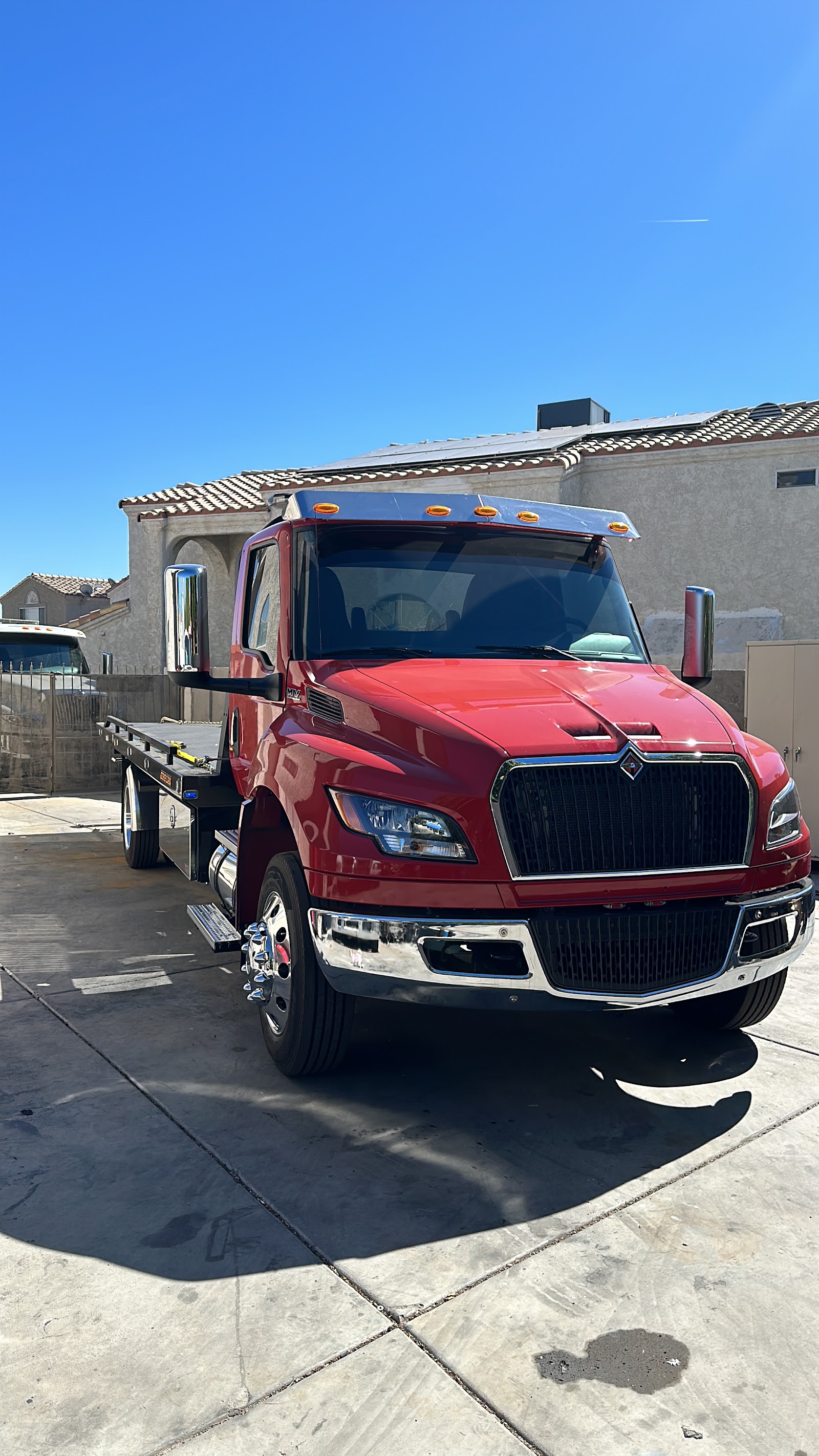 Red International flatbed tow truck parked on a residential driveway under clear blue sky